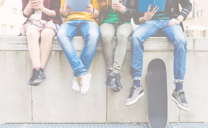 Four people sitting on edge of concrete with legs dangling