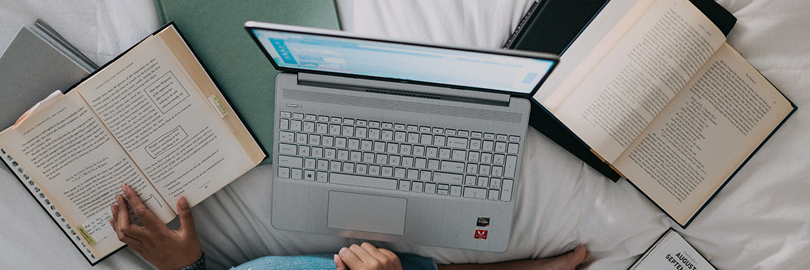 Woman sittign on bed with open laptop and several open textbooks