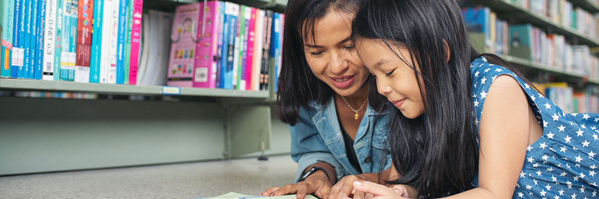 Mom and daughter on library floor reading a book together