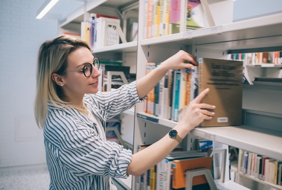 Adults landing page link image showing a woman picking a book from the shelf