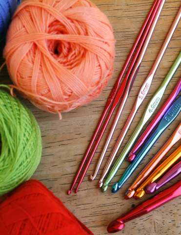 three skeins of yarn, 11 colorful crochet hooks to the right