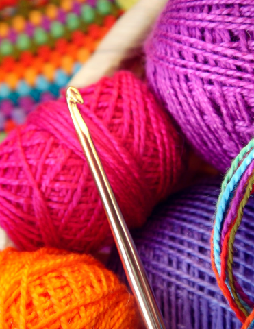 colorful crochet pattern in top left corner, four skeins of colorful yarn in right corner with crochet hook lying over the top of the skeins