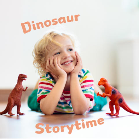 A young, blonde boy laying down on the floor with a smile on his face. He is surrounded by two miniature plastic dinosaur toys.