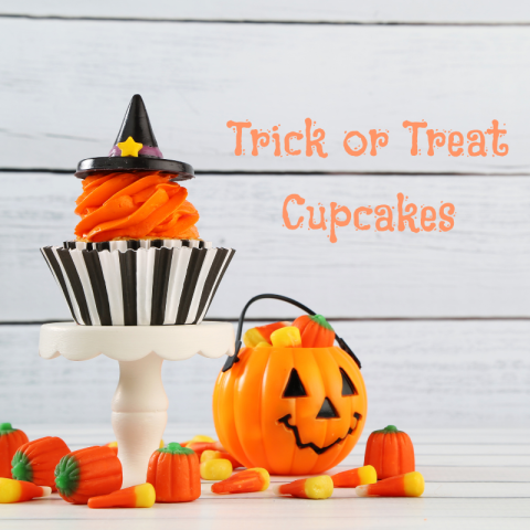 An orange cupcake on a display case, next to a jack-o-lantern shaped candy basket.