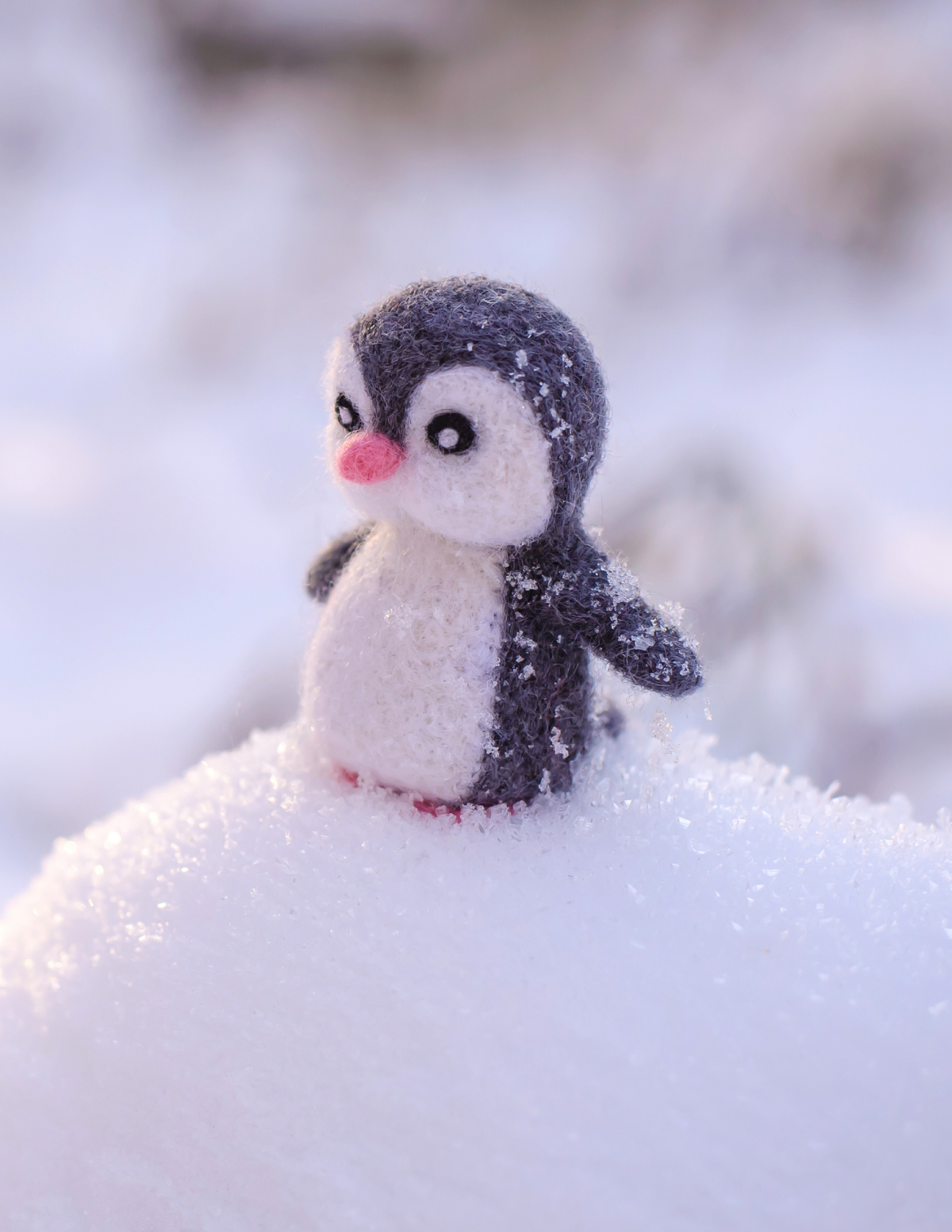 gray and white felted penguin on top of a mound of snow