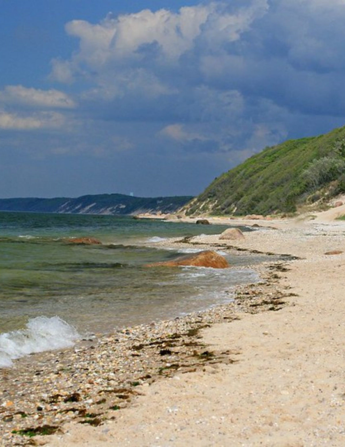 sandy beach green water small wave and green hills