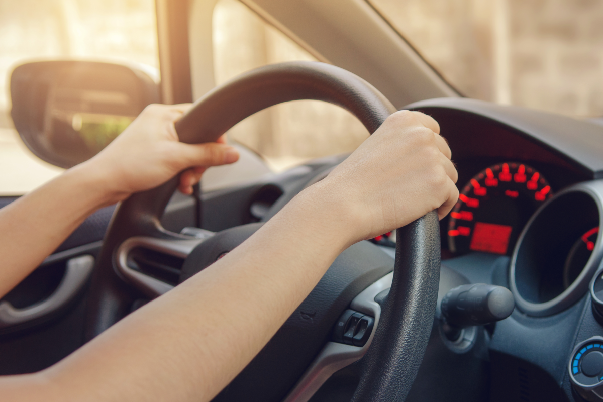 arms with hands gripping a steering wheel