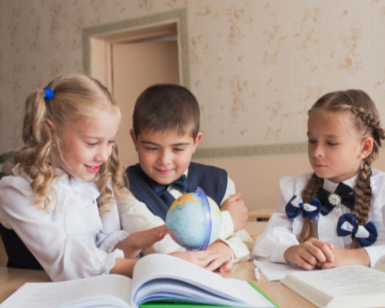 Three kids looking though books and at a globe