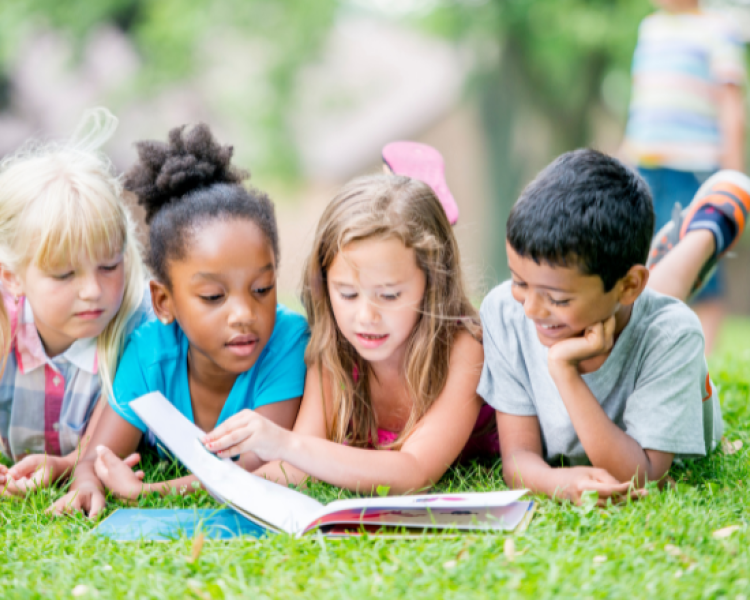 Four children reading a book in the grass